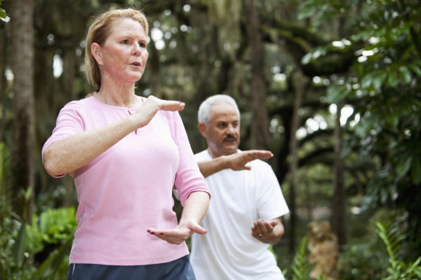 Multi-ethnic adults practicing tai chi in park. Focus on woman (50s).
