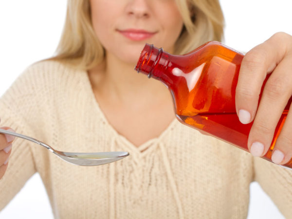 Woman getting ready to pour liquid from a bottle into a measuring spoon.