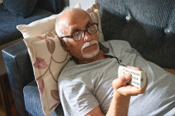 Senior man laying on couch with television remote.