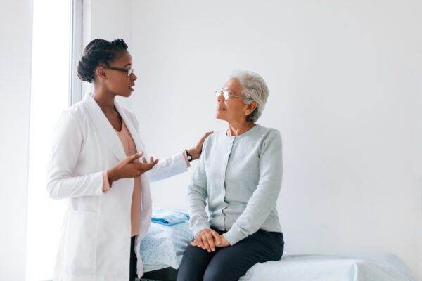 A black female doctor standing face to face with a senior female patient and talking to her in doctor's office.